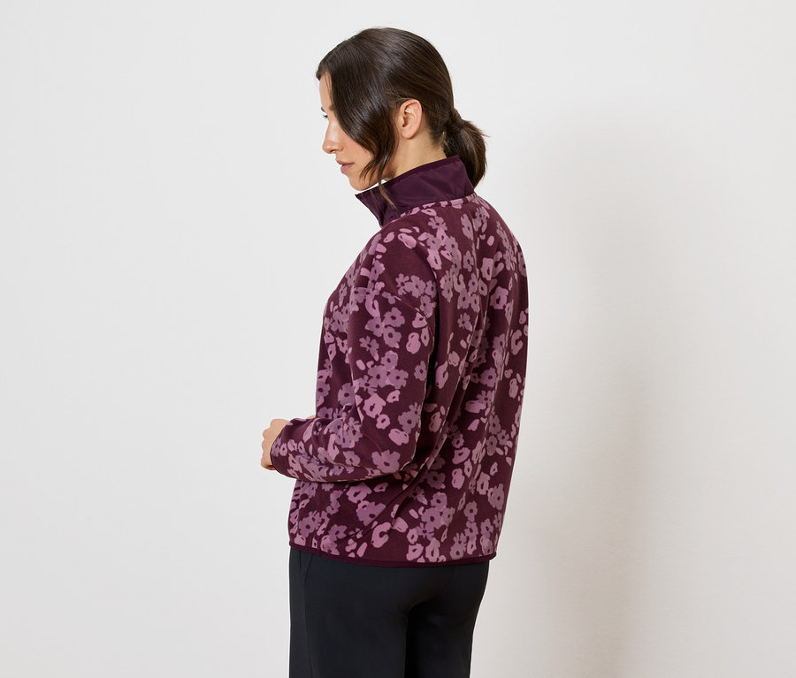 Frau in einer weinroten Jacke mit Blumenmuster, Seitenansicht.