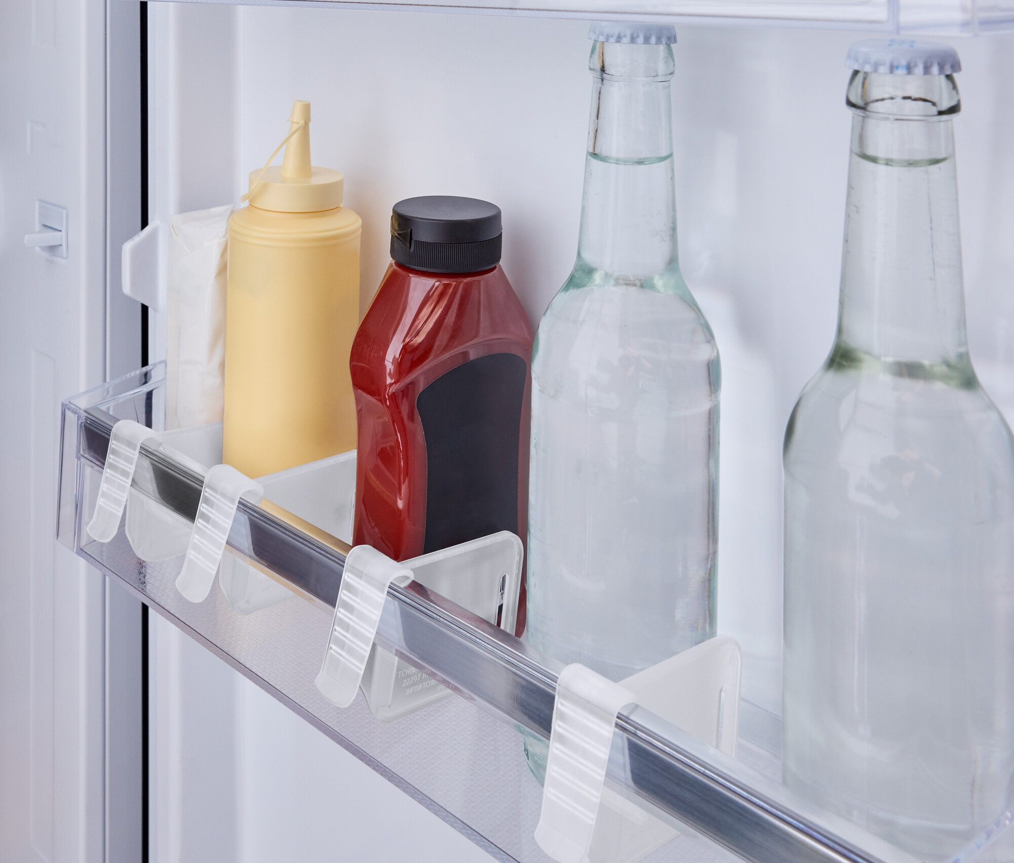 Im Kühlschrankregal stehen eine gelbe Senfflasche, eine rote Ketchupflasche und zwei Glasflaschen mit Wasser.