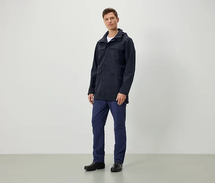 Ein Mann steht und trägt eine dunkelblaue Jacke mit Kapuze, dunkelblaue Hosen und schwarze Schuhe.