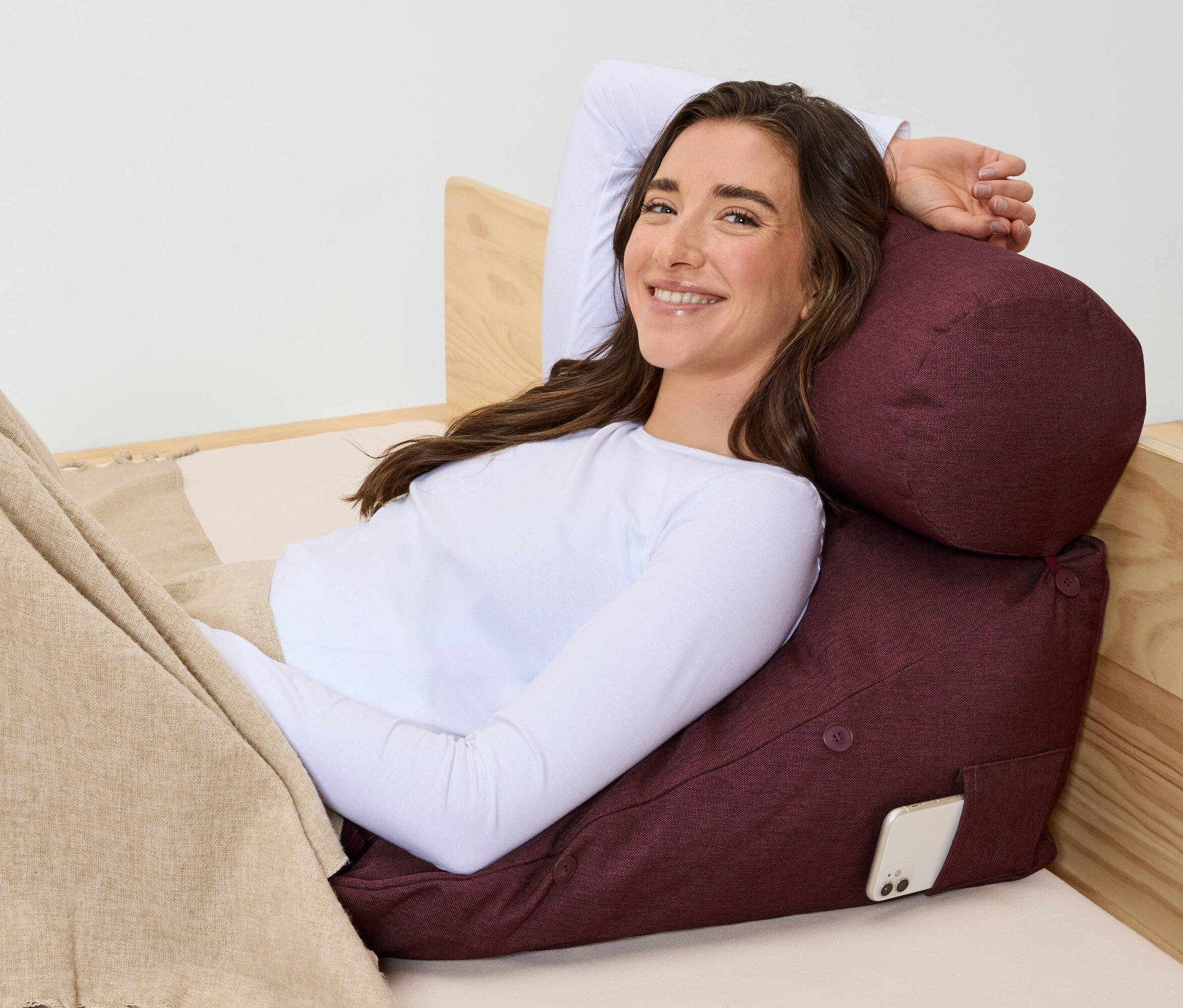 Frau liegt im Bett und stützt sich auf ein bordeauxrotes Kissen mit einem Telefon in der Tasche.