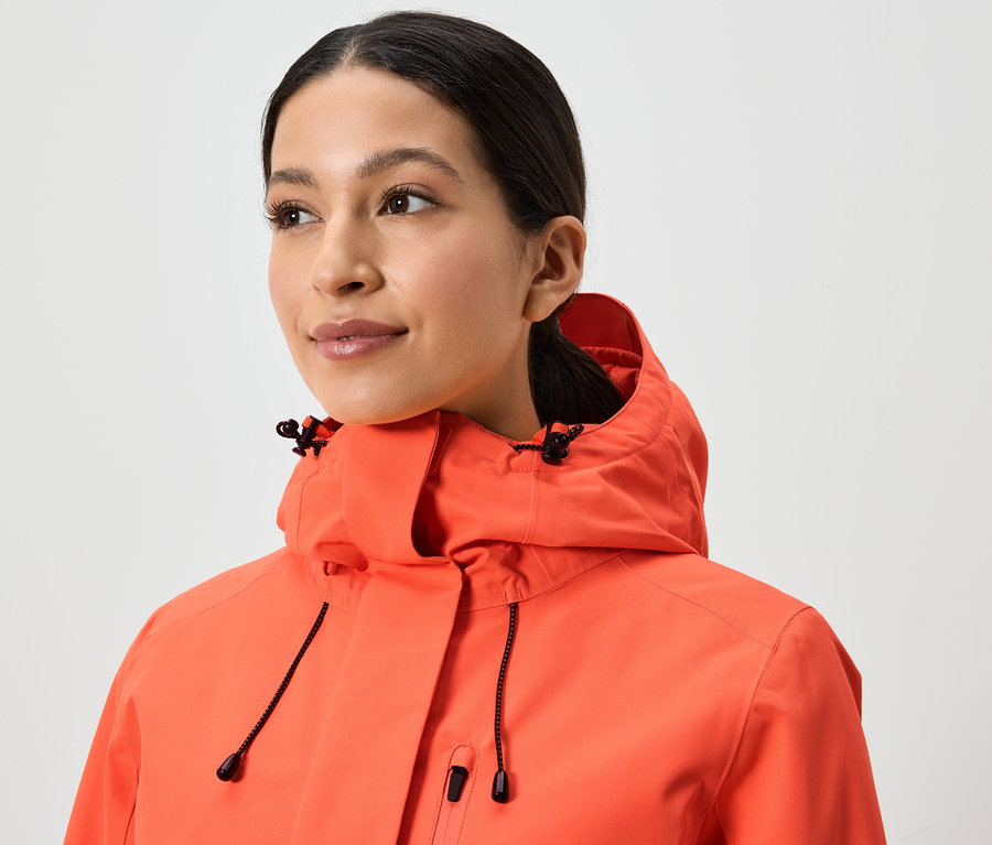 Porträt einer Frau in einer korallenroten Jacke mit Kapuze.