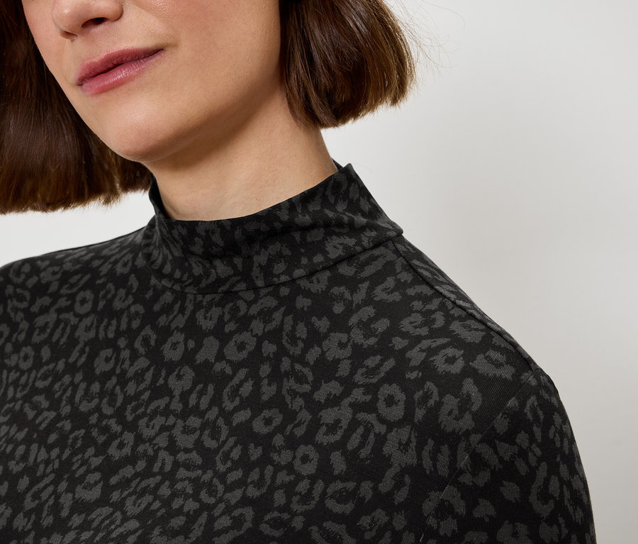 Detailaufnahme vom Oberkörper einer Frau, die einen schwarz-grauen Rollkragenpullover mit Leopardenmuster trägt.