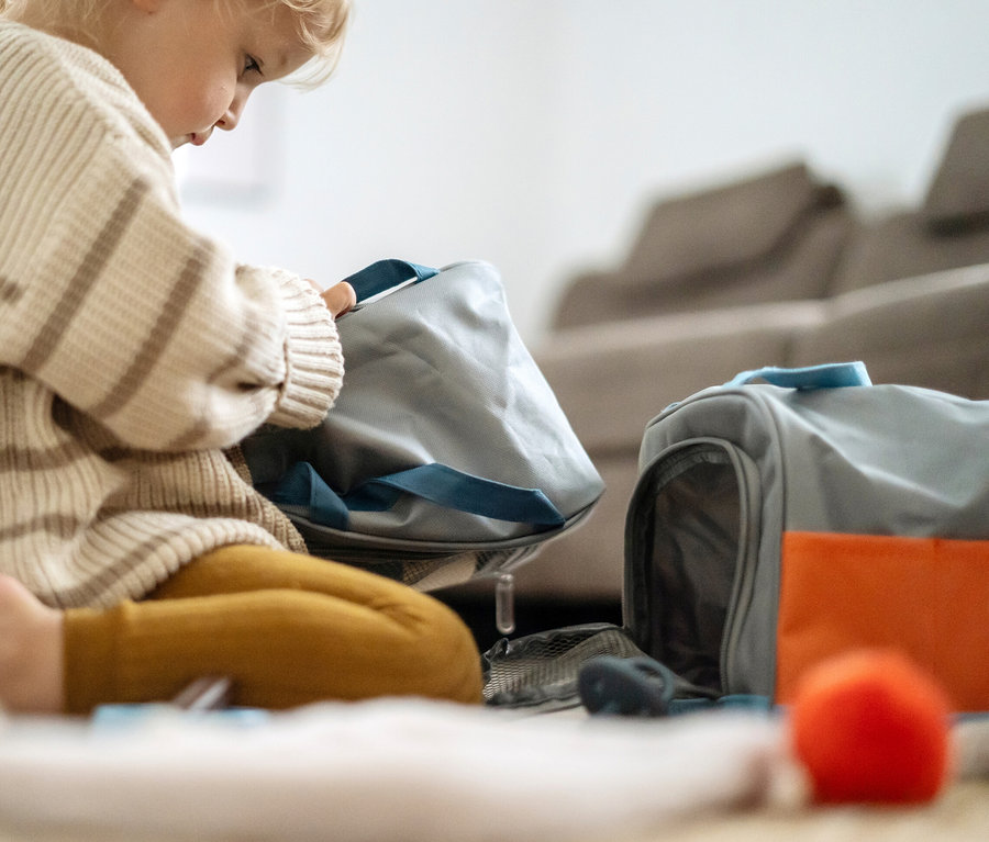 Kind sitzt am Boden und spielt mit einer grauen Tasche und Spielzeug, darunter ein 'small foot Katze mit Tasche und Pflege-Set'.