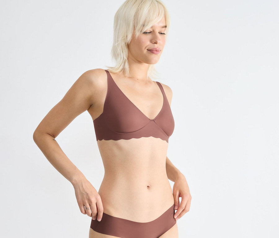 Blonde Frau trägt einen braunen sloggi ZERO Microfibre 2.0 Soft Bra und passende Höschen, Hände an den Hüften.