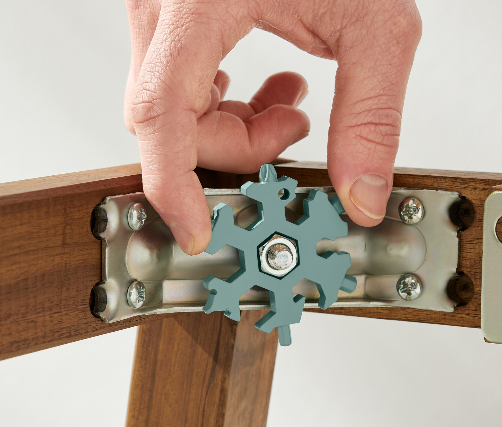 Eine Hand hält einen Multifunktionsschlüssel an einer Schraube an einem Holzrahmen.