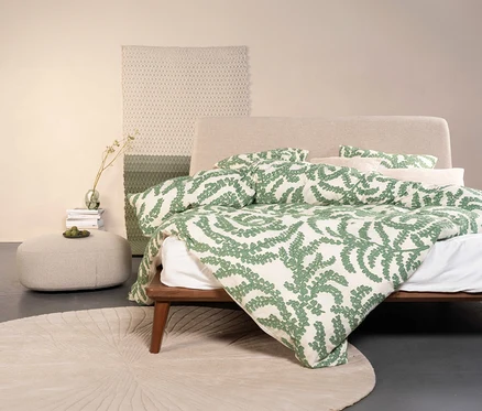 Bett mit Essenza Satin-Bettwäsche »Eleria« in Normal- und Übergröße mit grünem Blätterdruck, dazu Teppich, Hocker und Deko.