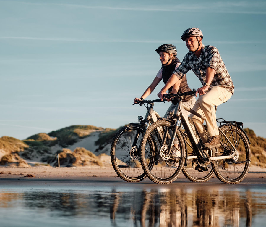 Zwei Personen fahren auf FISCHER Trekking-E-Bikes TERRA 2.2 ACTIVE (Trapez Rahmen) am Strand entlang.