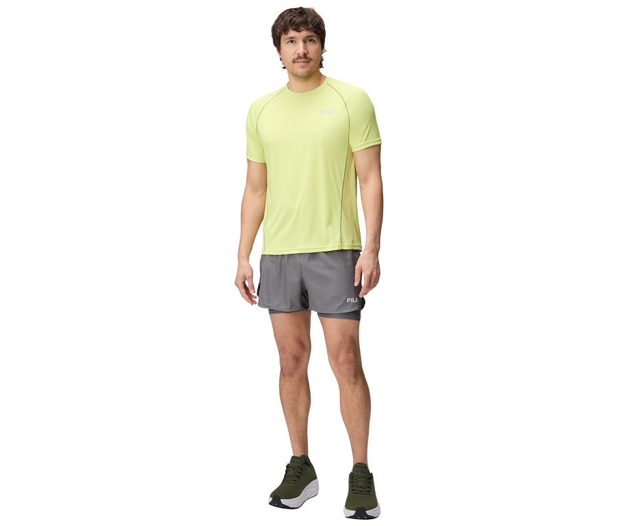 Mann steht und trägt ein gelbes T-Shirt, graue Shorts und grüne Schuhe.