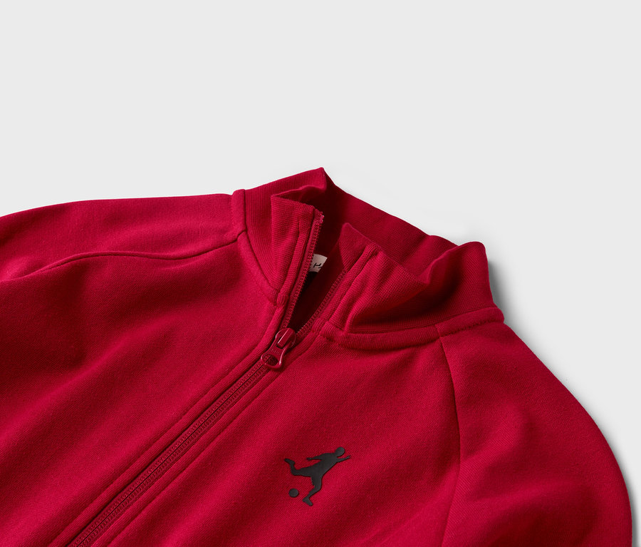 Nahaufnahme einer roten Trainingsjacke mit Reißverschluss und kleinem Fußballspieler-Logo.