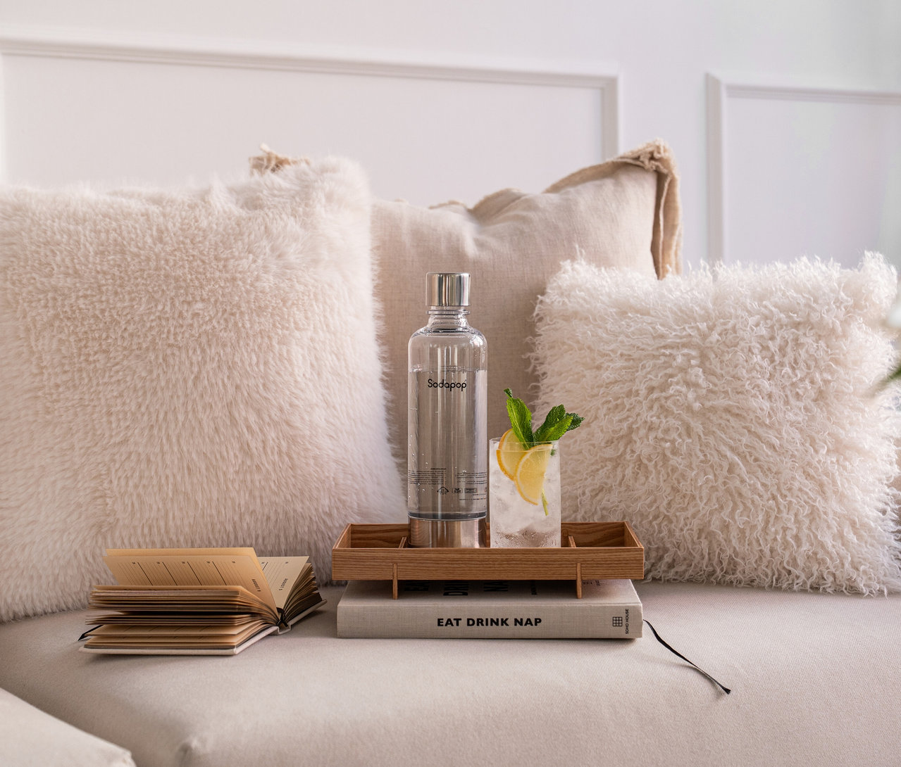 Sodapop Wassersprudler Cooper Pro, inkl. 5 Flaschen, schwarz, steht auf einem Tablett neben einem Drink und Kissen.