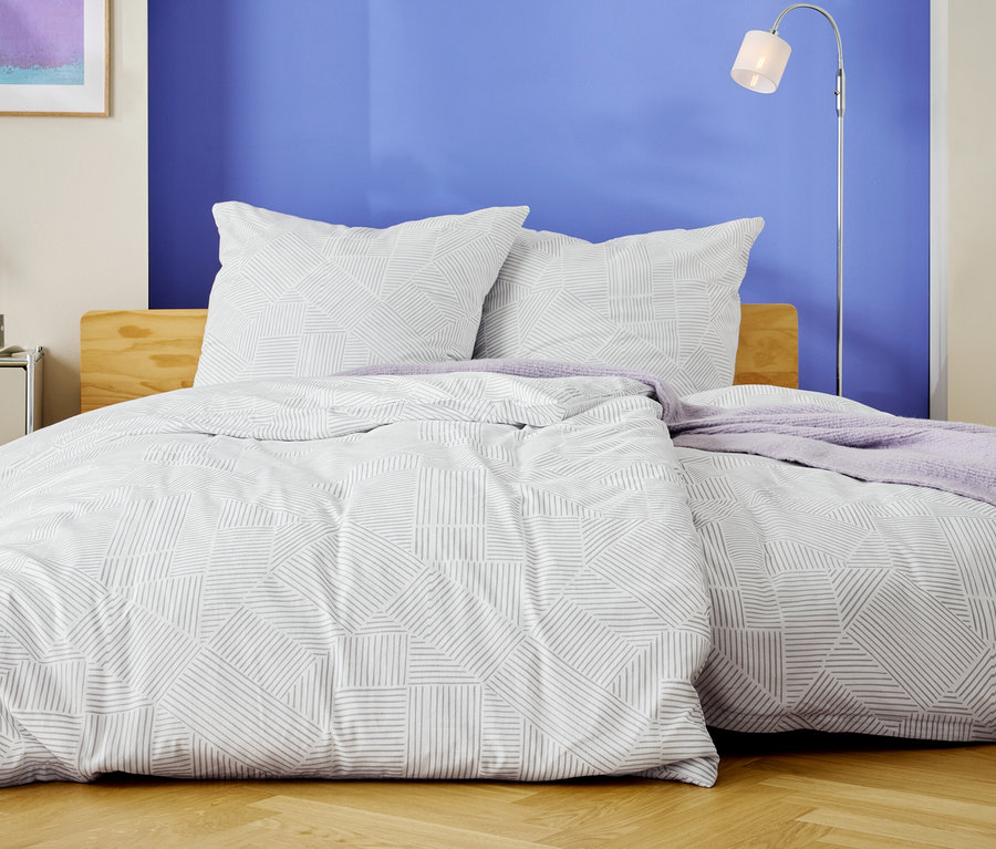 Ein Bett mit weißer Bettwäsche mit geometrischem Muster und zwei Kissen steht vor einer blauen Wand.