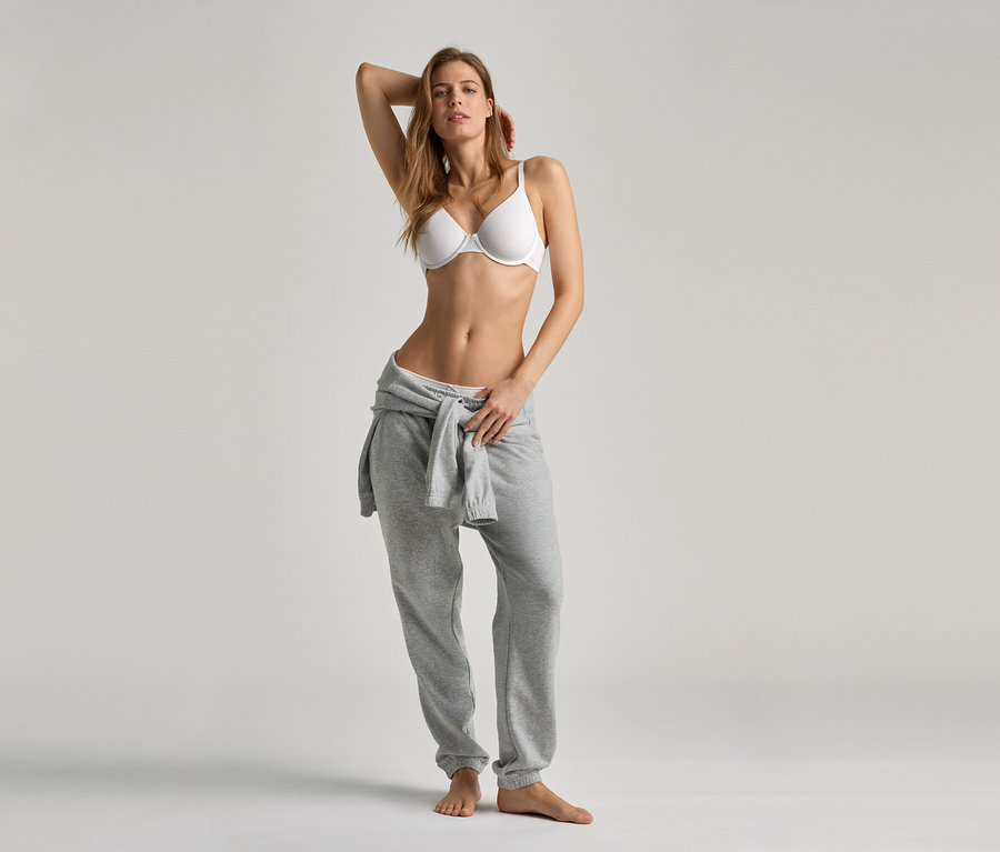 Frau posiert in weißem BH und grauer Hausanzugshose.