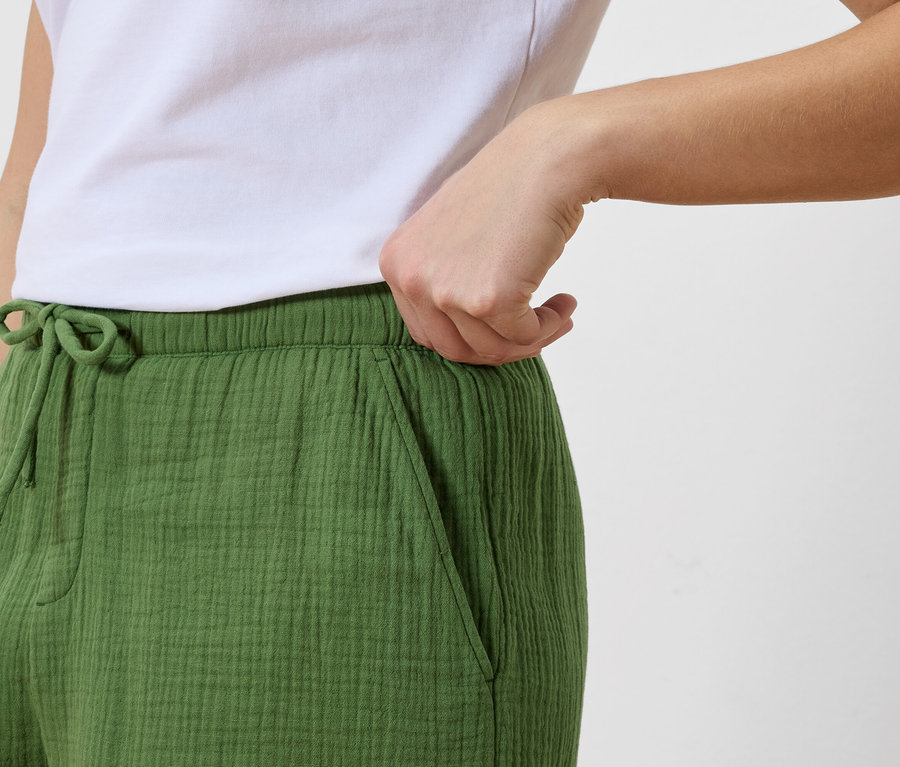 Frau greift in die Tasche einer grünen Hose mit Kordelzug, dazu ein weißes T-Shirt.