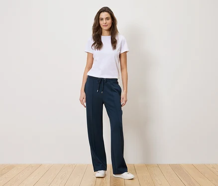 Frau steht und trägt ein weißes T-Shirt und eine marineblaue Hose.