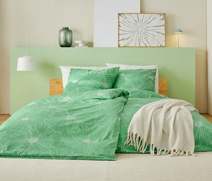 Ein Bett mit grünem Bettbezug mit weißem Blumenmuster, einer weißen Decke und einem hellgrünen Kopfteil.