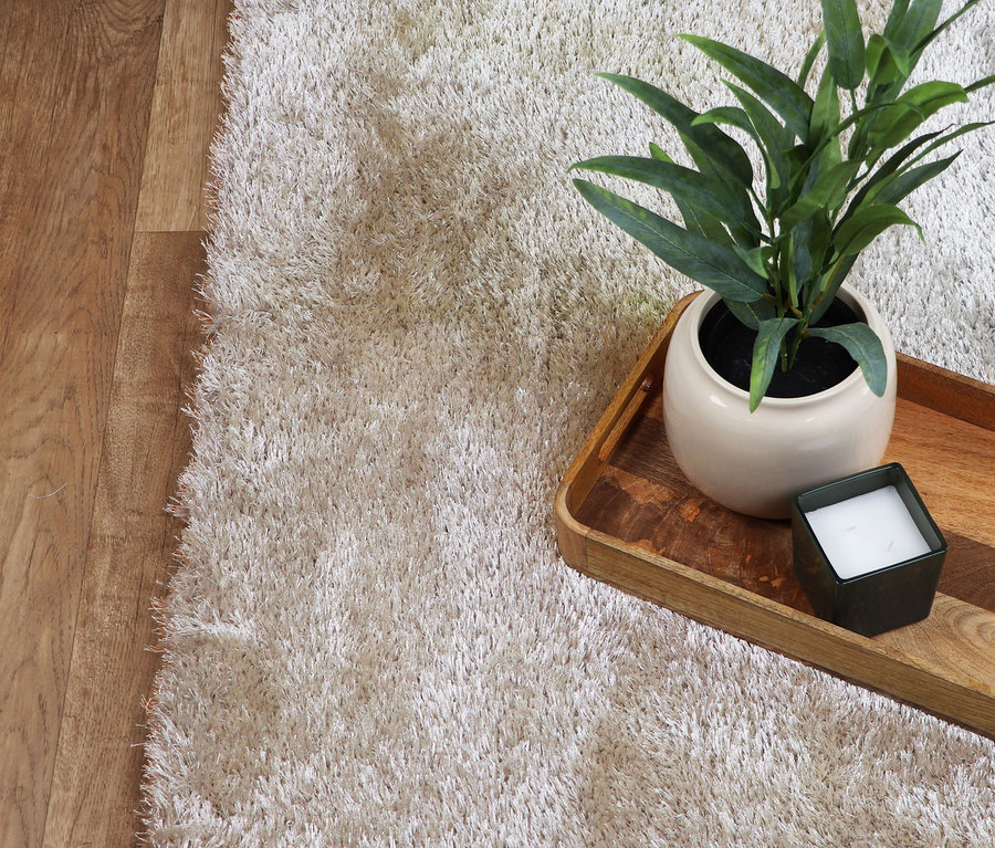Nahaufnahme eines cremefarbenen »Silky« Teppichs mit einer Topfpflanze und einer Kerze auf einem Holztablett.
