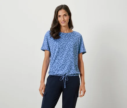 Frau trägt ein blaues T-Shirt mit Muster und marineblaue Hosen.