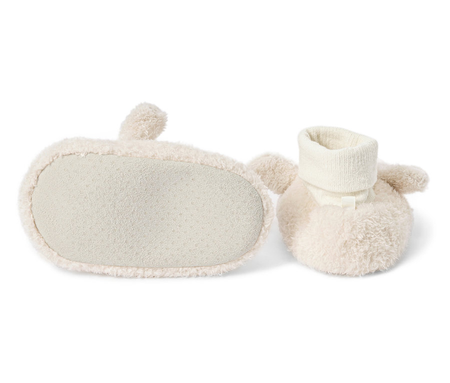 Zwei cremefarbene Baby-Booties, einer mit Blick auf die Sohle, liegen auf einem weißen Hintergrund.