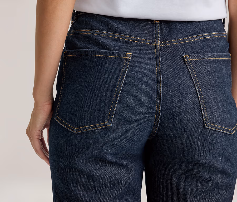 Person von hinten in dunkelblauer Jeans mit sichtbaren Gesäßtaschen und gelben Nähten.