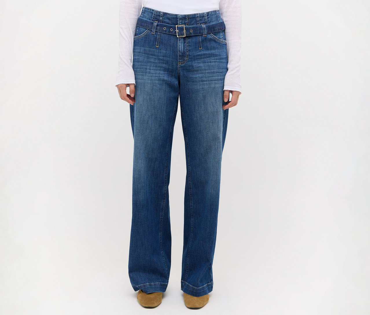 Person trägt hochgeschnittene, weite blaue Jeans mit passendem Jeansgürtel und rechteckiger Schnalle, dazu ein weißes Langarmshirt und braune Schuhe.