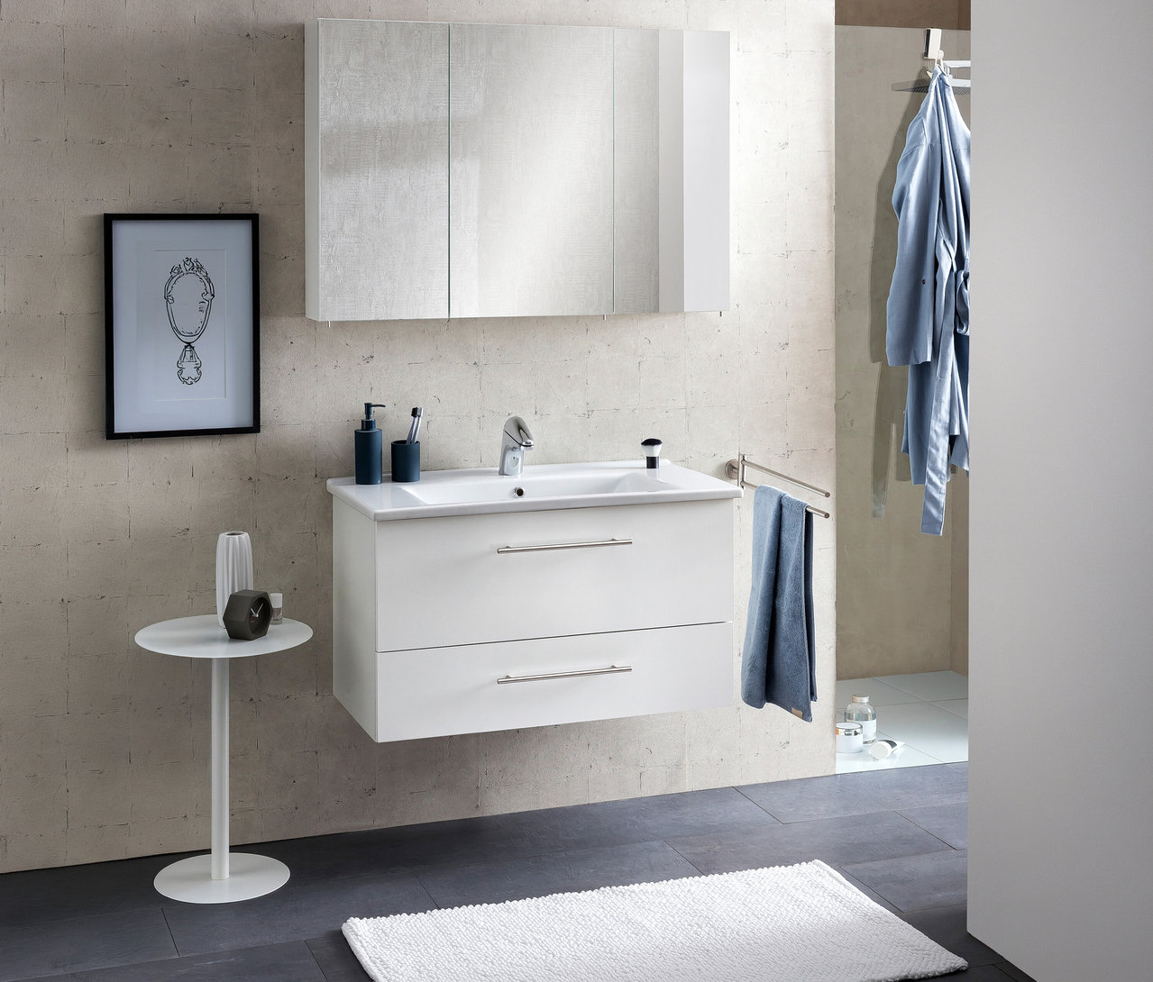 Modernes Badezimmer mit weißem Waschtischunterschrank, integriertem Waschbecken und einem Spiegelschrank »Basic«, 100 cm, darüber. Ein blaues Handtuch hängt rechts, ein Bademantel an der Wand.