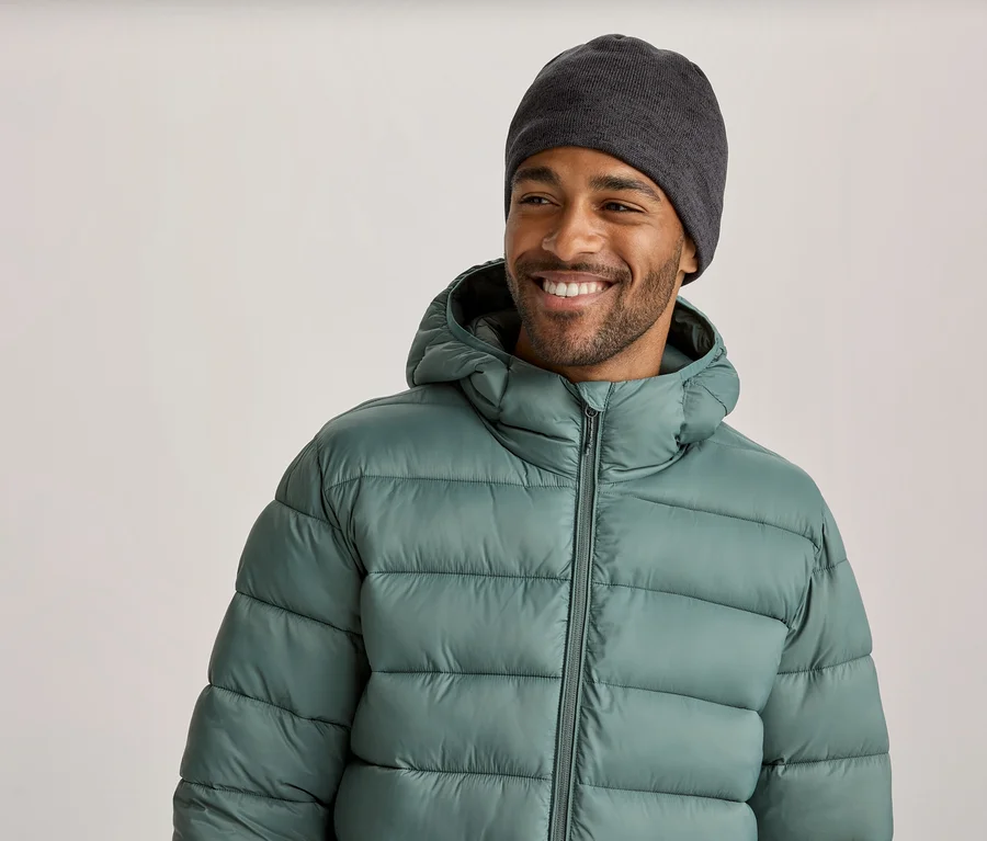 Ein lächelnder Mann mit dunkelgrauer Mütze und hellgrüner Steppjacke mit Kapuze blickt nach rechts.