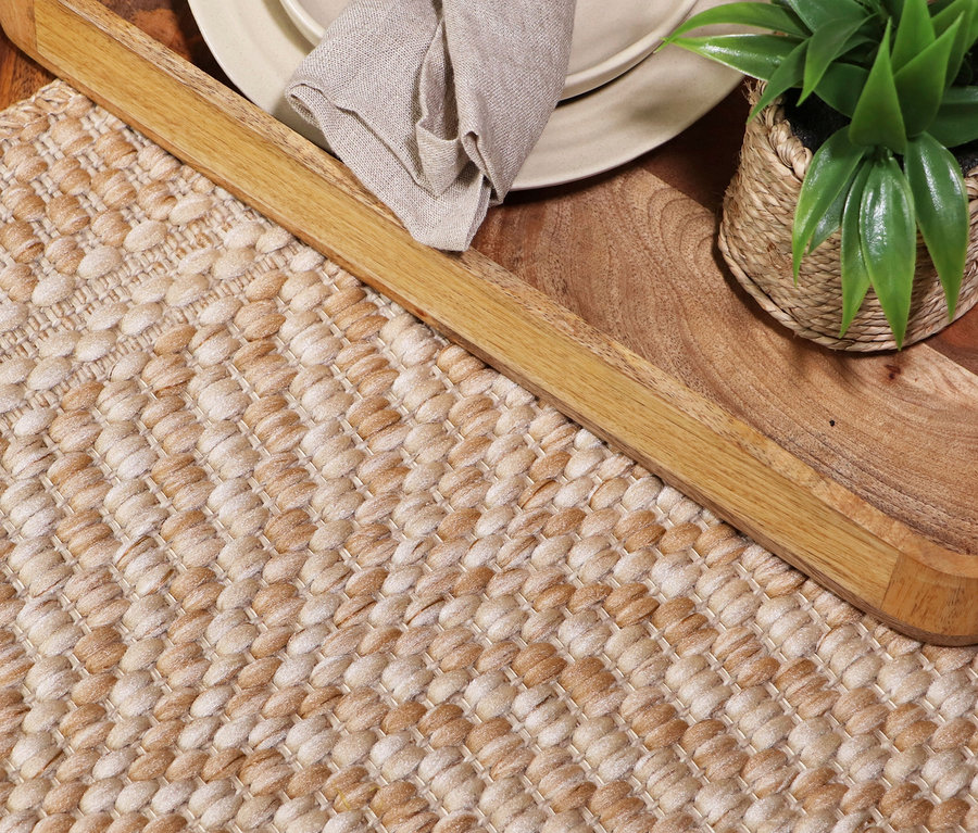 Nahaufnahme eines Teppichs »Twine« mit Fischgrätmuster in Beige- und Brauntönen, daneben ein Holztablett mit Geschirr und einer Pflanze.