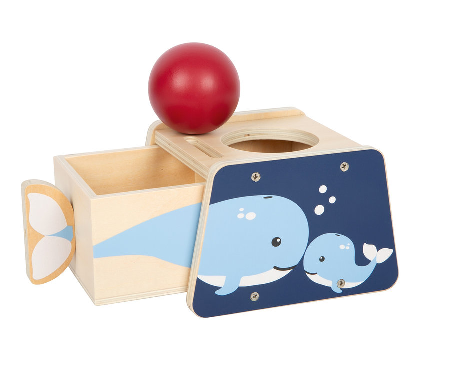 Holzspielzeugkiste mit rotem Ball auf einem Loch, herausgezogener Schublade und dunkelblauer Platte mit zwei blauen Walen.