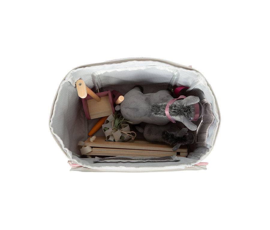 Eine offene hellgraue Tasche mit gestreiftem Futter, gefüllt mit dem small foot Spielset Esel mit Stall. Darin befinden sich zwei graue Plüsch-Esel, Holzteile für einen Stall, eine rosa Holzschubkarre, eine Spielzeugkarotte und eine kleine grüne Pflanze.