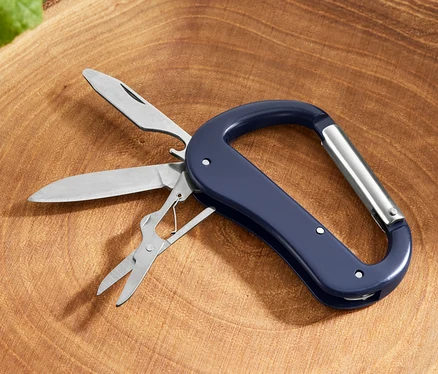 Ein 5-in-1-Karabiner-Multitool mit Messer, Säge und Schere liegt auf einem Baumstumpf.