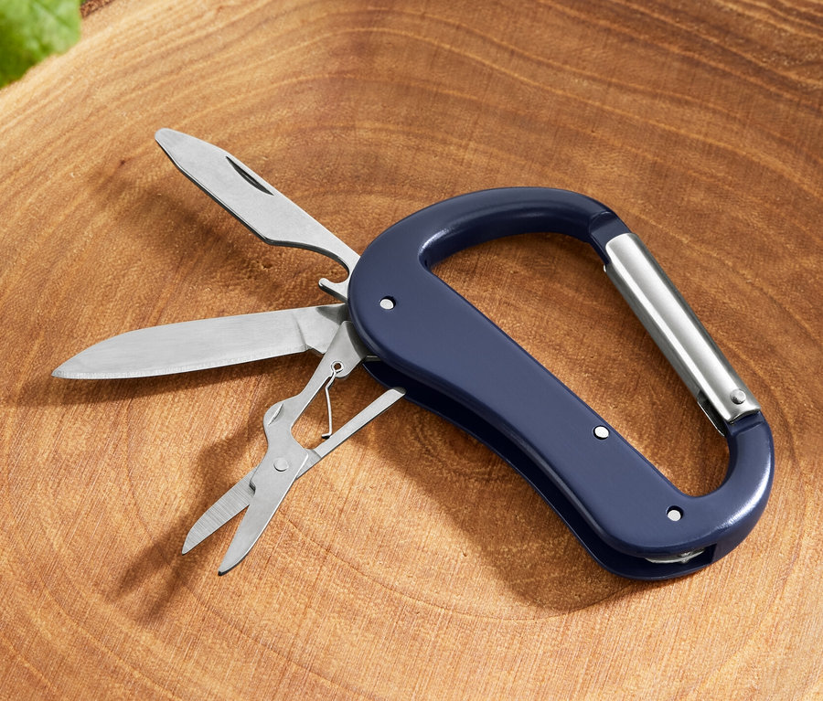 Ein 5-in-1-Karabiner-Multitool mit Messer, Säge und Schere liegt auf einem Baumstumpf.