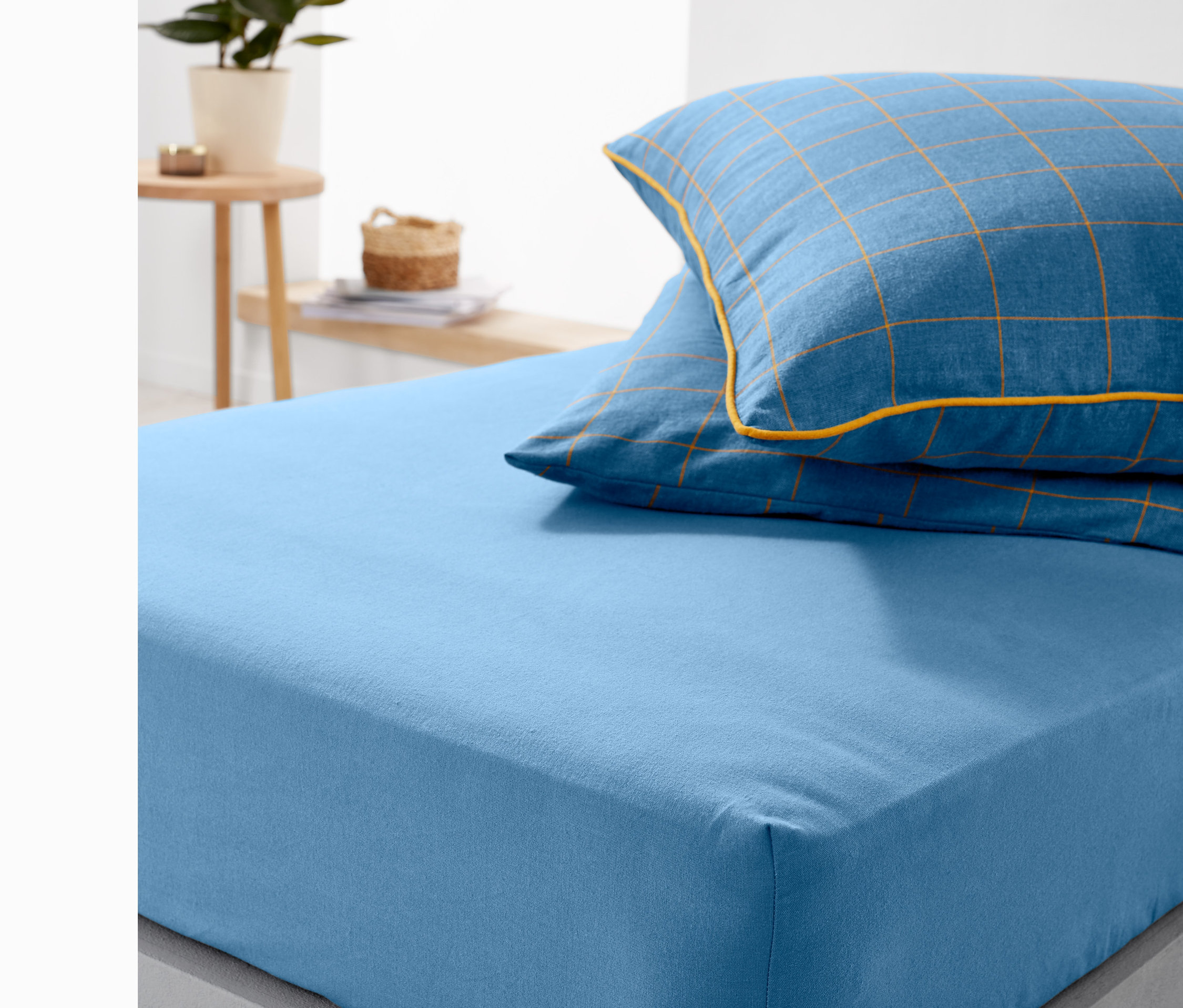 Blaues Biber-Spannbettlaken Normalgröße auf einem Bett, mit blau kariertem Kissen.