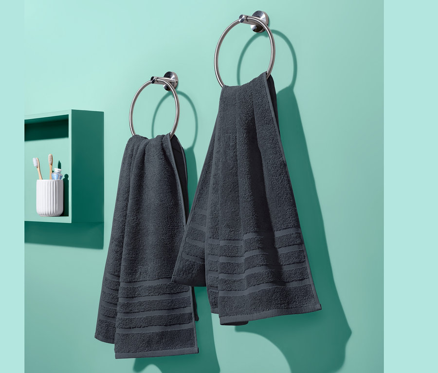 Zwei anthrazitfarbene Frottier-Handtücher hängen an runden Halterungen an einer blaugrünen Wand. Links ist ein kleines Regal mit Zahnbürsten.