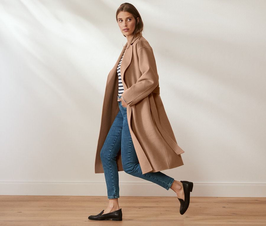 Frau geht, trägt Wollmantel mit Cashmere, Jeans und Slipper.