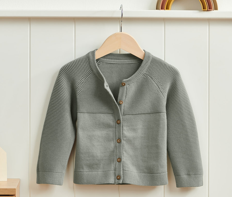 Eine grüne Strickjacke hängt an einem Bügel.