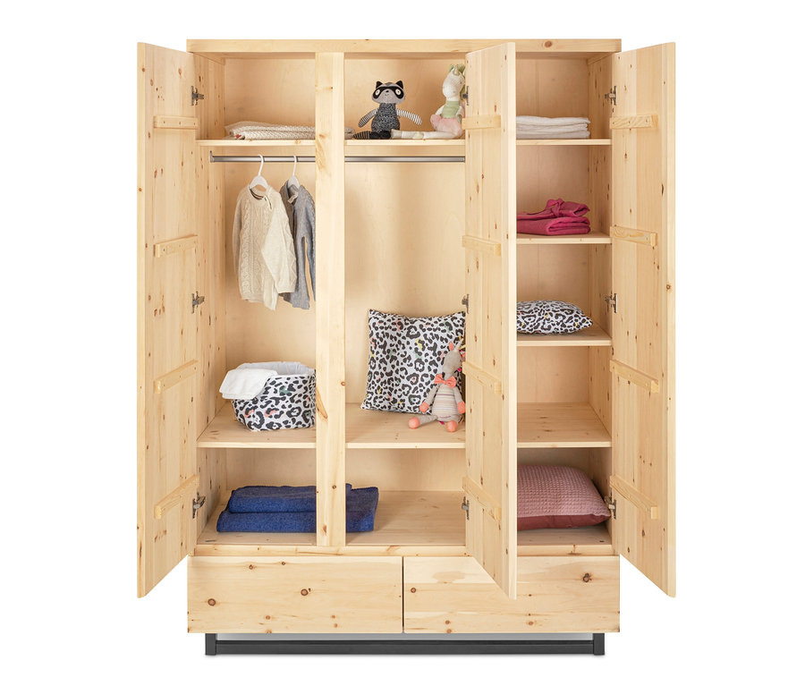 Geöffneter dreitüriger Schardt Schrank »Zirbenholz« mit Kleidung, Spielzeug und Kissen.