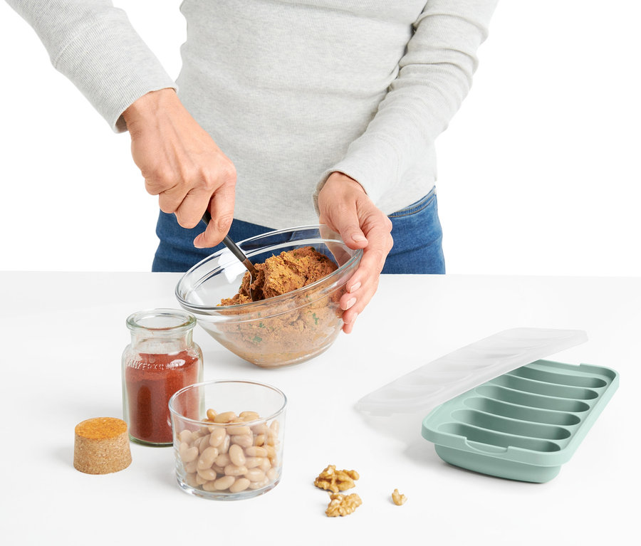 Frau rührt mit Löffel Zutaten in Schüssel neben Mikrowellen-Veggie-Würstchen-Bereiter.