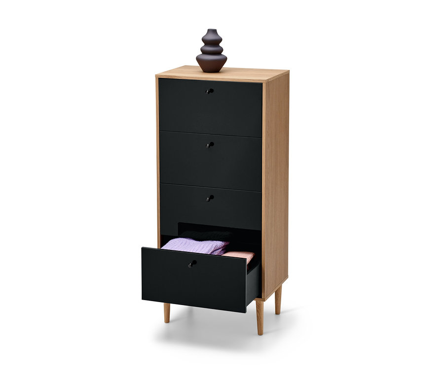 Schmale, anthrazitfarbene Kommode »Bekeson« mit vier Schubladen, von denen eine offen ist und gefaltete Pullover enthält. Auf der Kommode steht eine braune Vase.