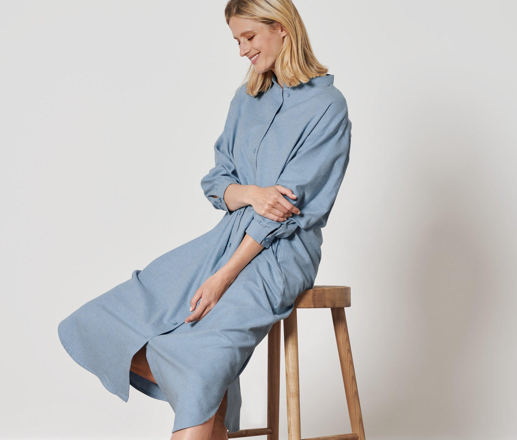 Frau sitzt auf einem Holzhocker und trägt ein Flanell-Nachthemd.