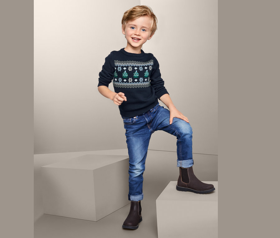 Junge posiert in einem Strickpullover mit Weihnachtsbäumen.