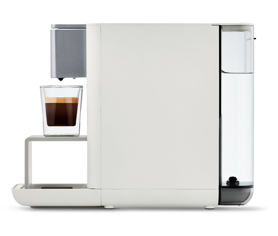 Qbo ESSENTIAL Bright Sand Kaffeemaschine mit einer Tasse Kaffee.