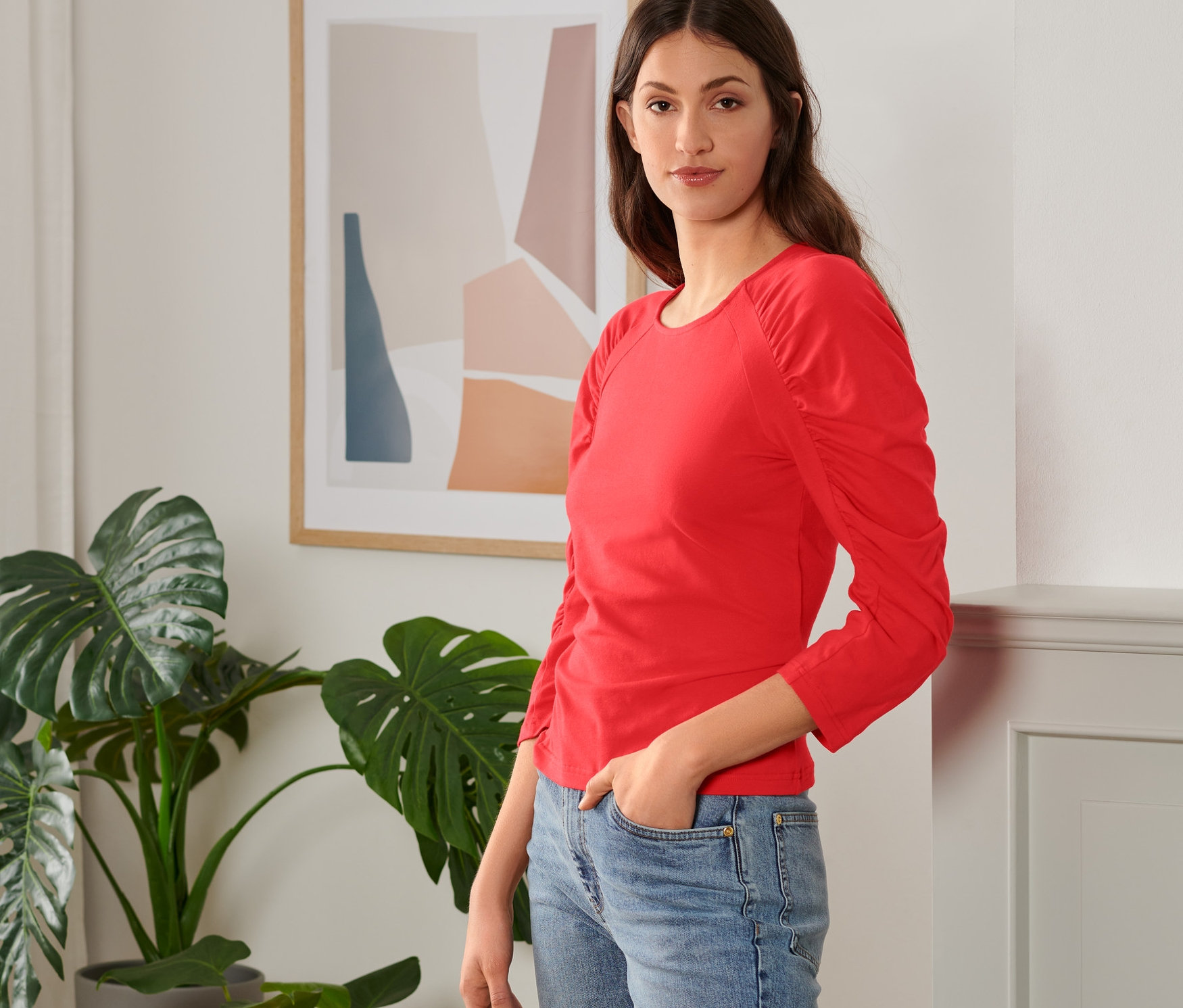 Frau posiert in rotem Shirt mit 3/4-Arm und blauen Jeans.