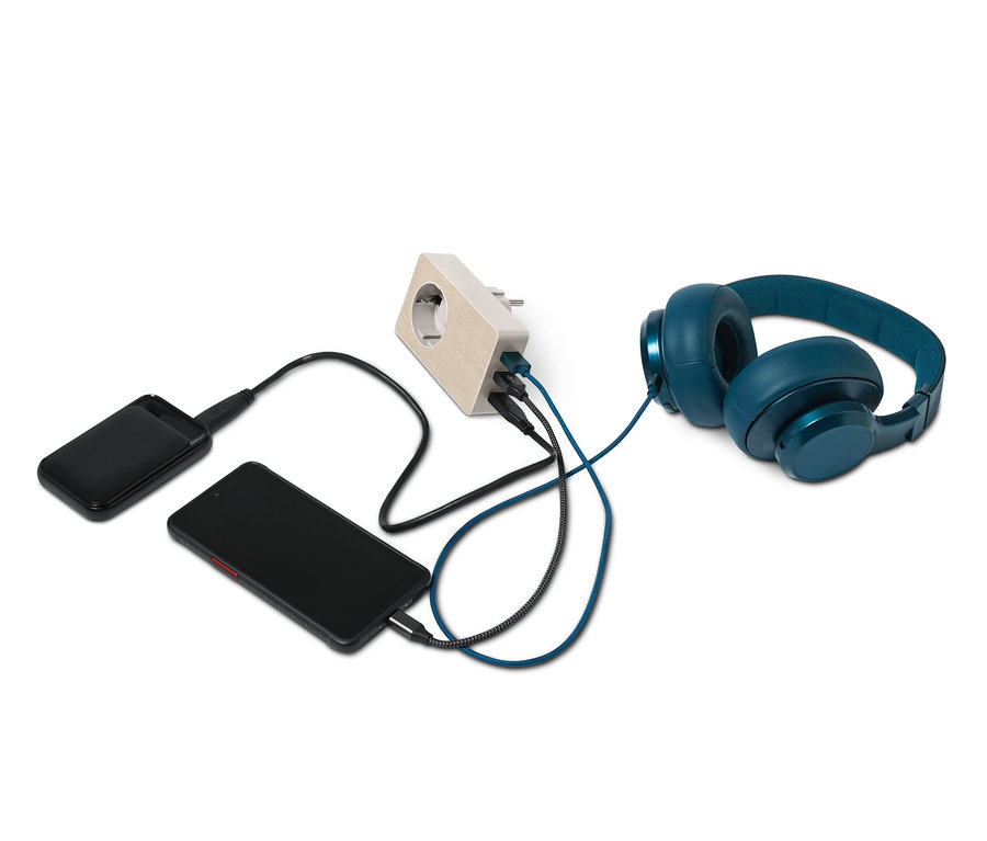 Ein schwarzes Telefon, eine Powerbank und blaue Kopfhörer werden mit einem 4-in-1-USB-Steckdosen-Adapter aufgeladen.