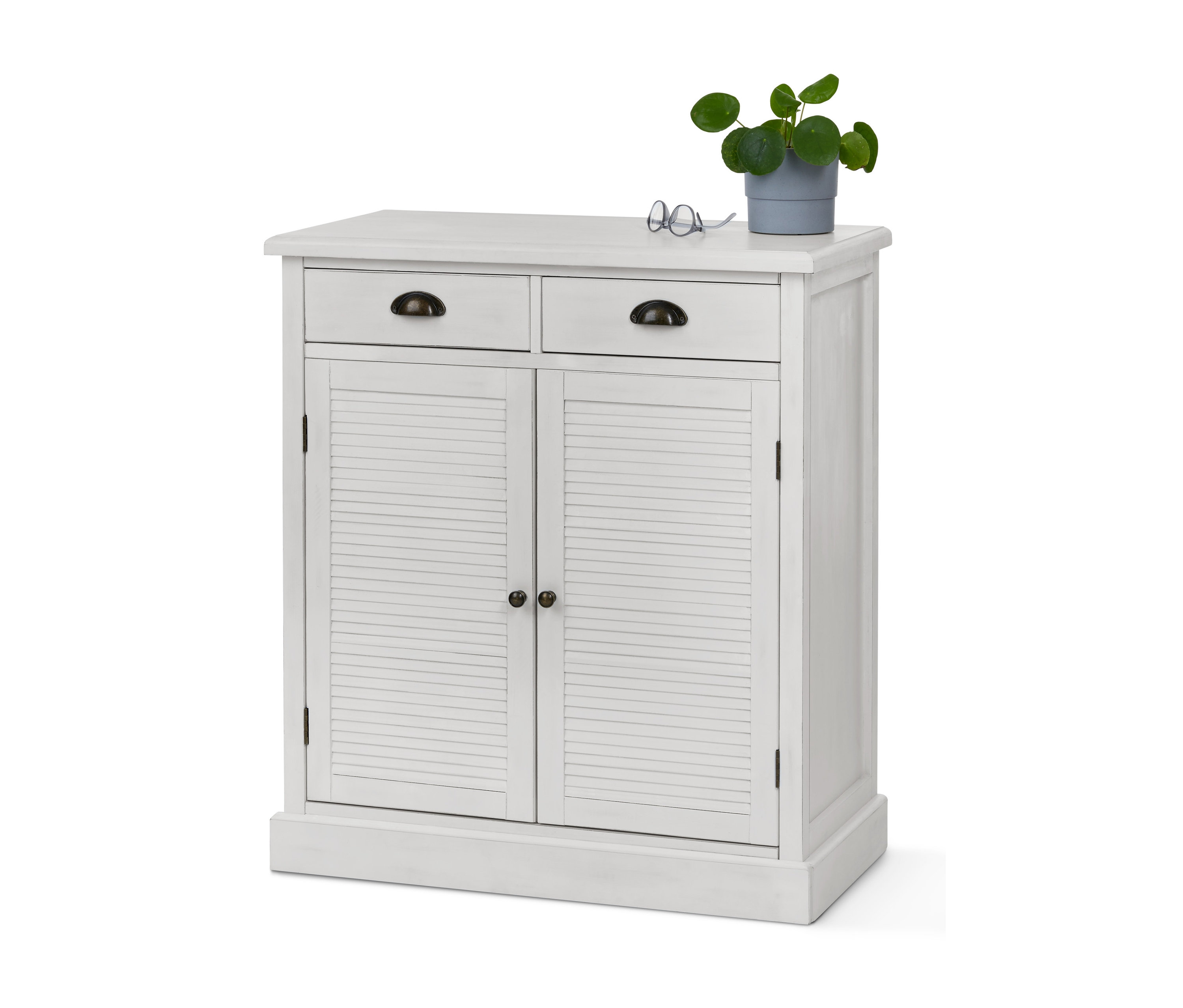 Weiße Kommode mit Lamellentüren, zwei Schubladen, Brille und Topfpflanze.