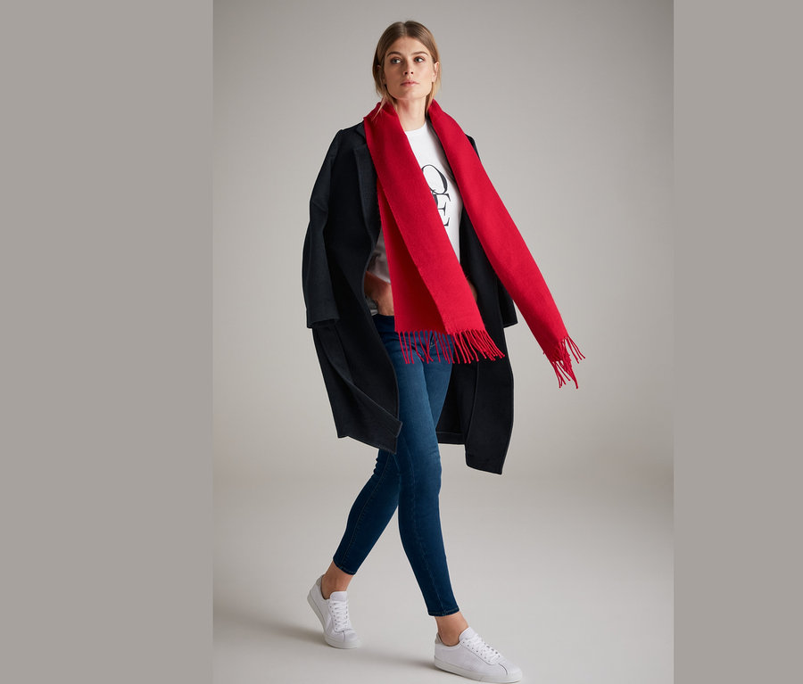 Frau posiert in Skinny-Jeans und rotem Schal mit Fransen.
