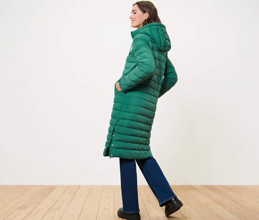 Frau posiert seitlich in einem langen Steppmantel mit Kapuze.