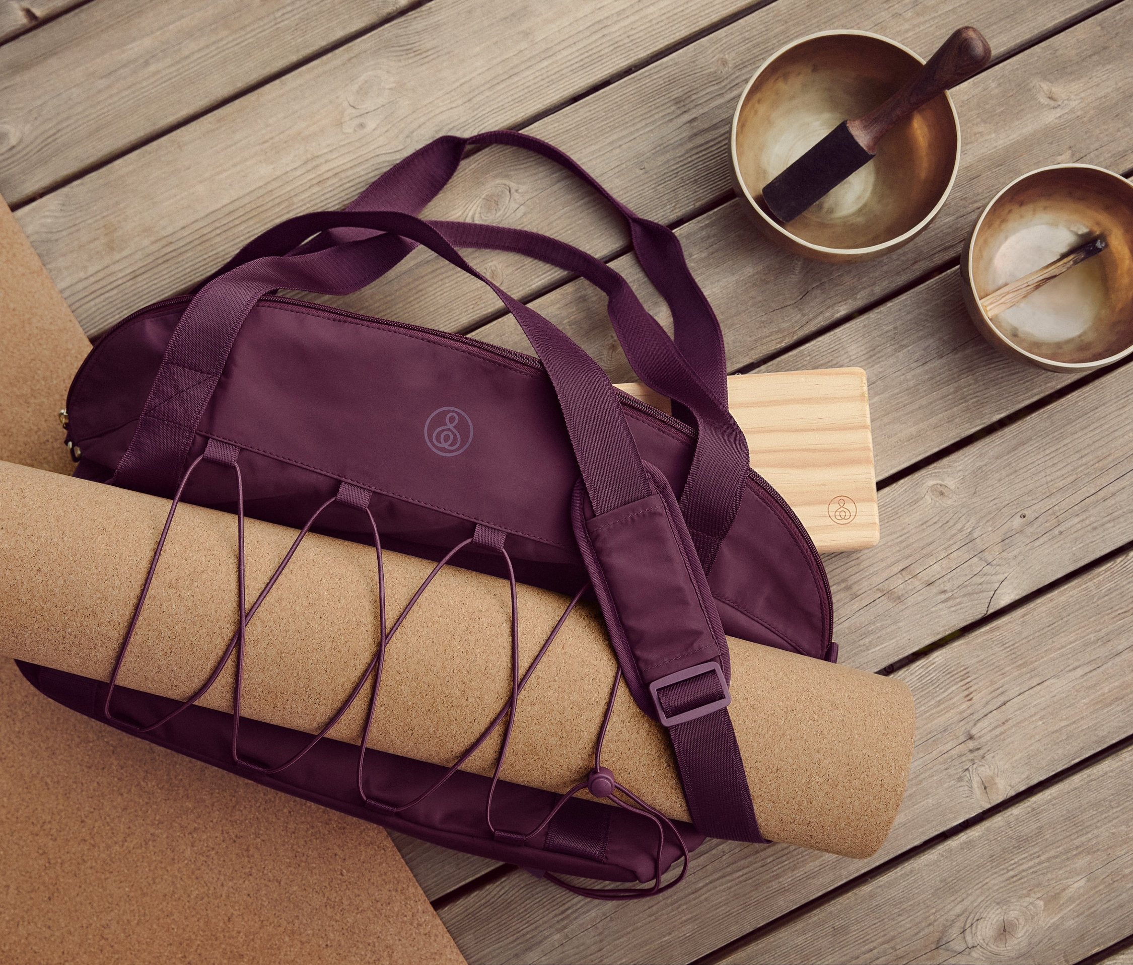 Auf einem Holzboden liegen eine Kork-Yoga-und-Fitnessmatte, eine Sporttasche, ein Yoga-Block und zwei Klangschalen.