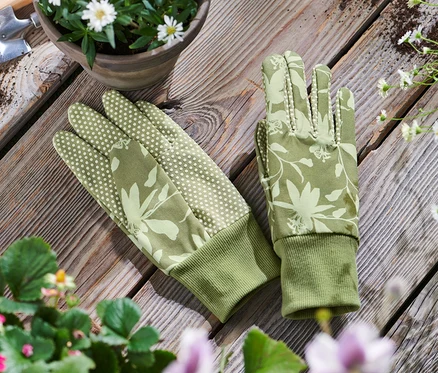 Garten-Handschuhe liegen auf einem Holztisch neben einem Blumentopf und Gartengeräten.