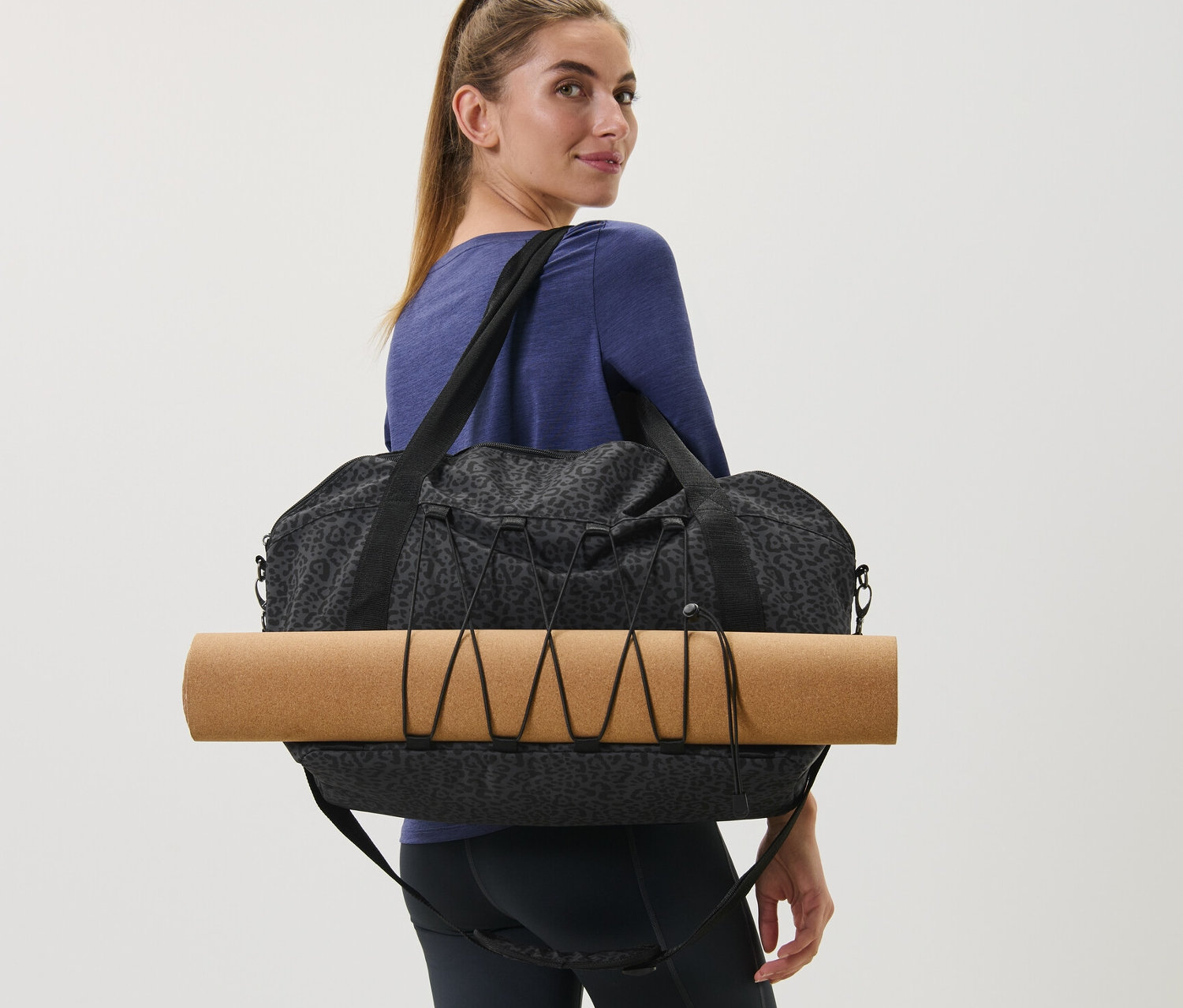 Frau trägt eine Sporttasche mit Alloverprint und eine Yogamatte.