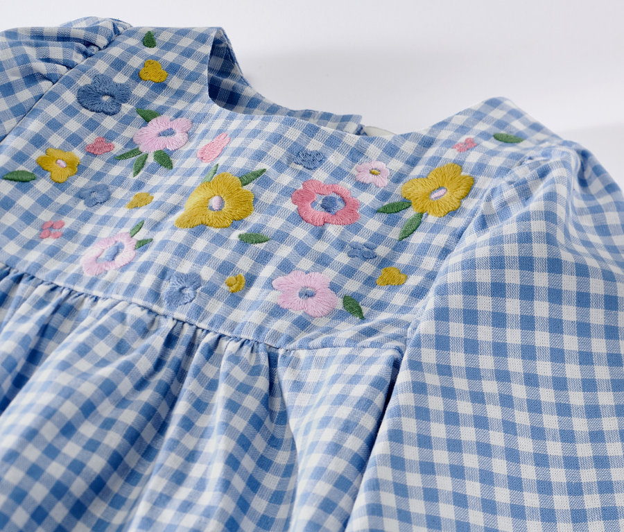 Detailansicht eines Kinder-Webkleids mit blau-weißem Karomuster und Blumenstickerei.